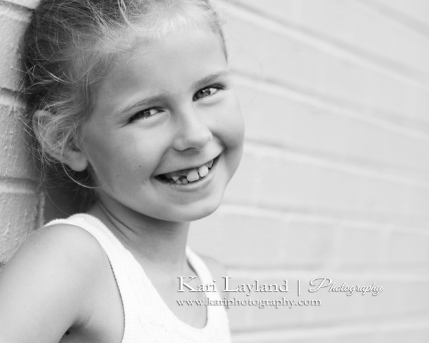 girl smiling by brick wall black and white portrait