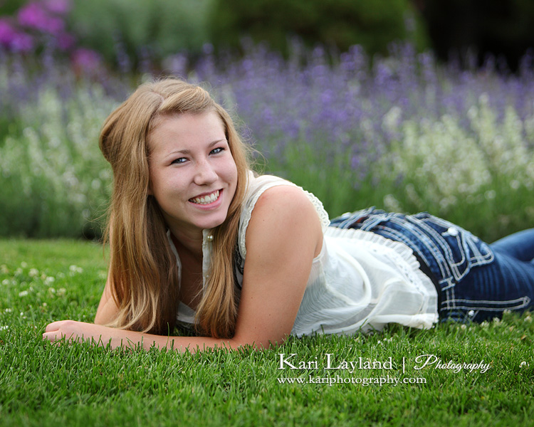Senior portrait of a girl laying on her belly in the grass, smiling with her hand in her hair.